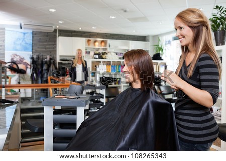 Young female hairdresser standing behind customer\'s chair after giving a haircut