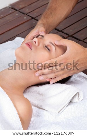 Beautiful young female receiving head massage by a male masseuse at health spa