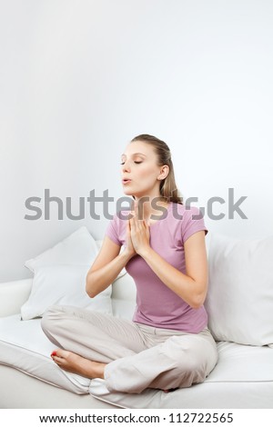 Young woman in casual wear meditating with hands clasped on sofa at home