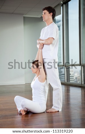 Yoga instructor teaching yoga positions to young woman at gym