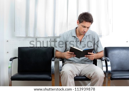 Young man reading book in doctor\'s waiting room