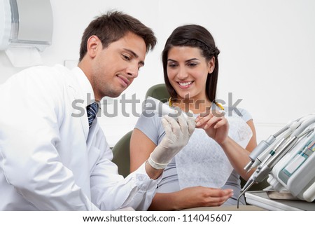Happy young male dentist prescribing tooth paste to female patient in clinic