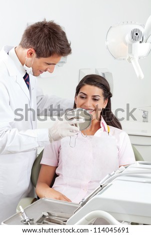 Young male dentist showing the result of his work to the satisfied patient