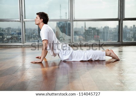 Side view of a young man doing Upward Facing Dog pose at gym