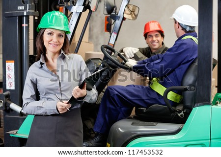 Portrait of smiling female supervisor with foremen communicating at warehouse