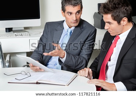 Two businessmen using digital tablet at desk in office