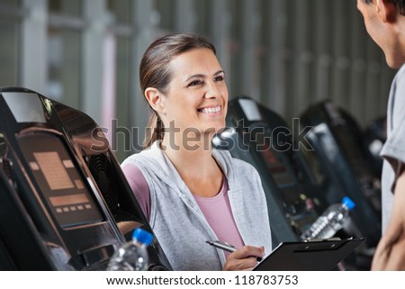 Happy female instructor looking at male client exercising on treadmill in health center