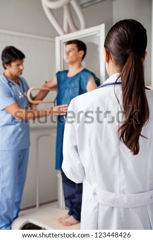 Rear view of female doctor with technician assisting patient for x-ray in background