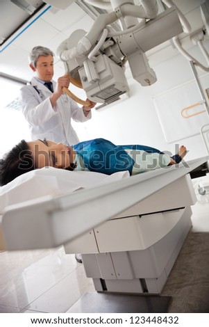 Mature male doctor setting up the machine to x-ray mid adult female patient