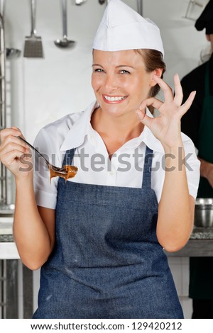 Portrait of happy female chef holding spoon with chocolate showing okay sign