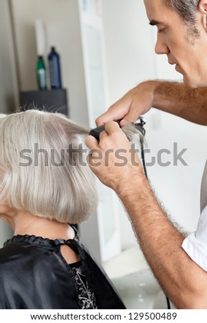 Male hairstylist straightening female customer\'s hair at beauty parlor