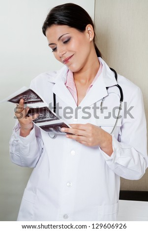 Pretty female radiologist smiling while looking at ultrasound print