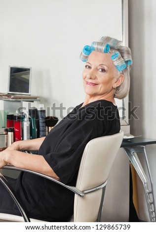 Portrait of senior woman with hair curlers sitting on chair at salon