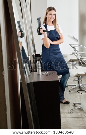 Portrait of female hairstylist with hair dryer in beauty salon