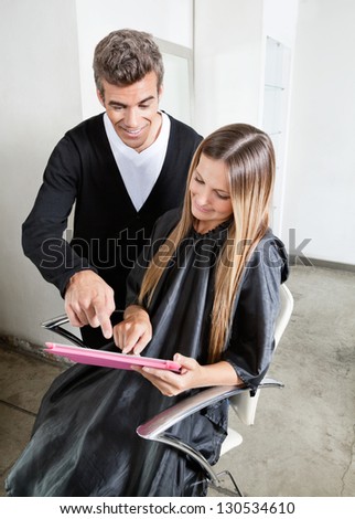 Hairstylist with female client using digital tablet at parlor