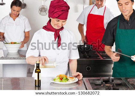 Female chef pouring oil in dish with colleagues working in commercial kitchen