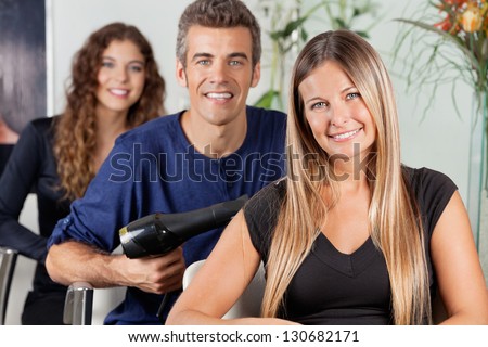 Portrait of attractive female hairdresser sitting with colleagues at beauty parlor