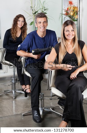 Portrait of confident hairstylists sitting on chairs in salon