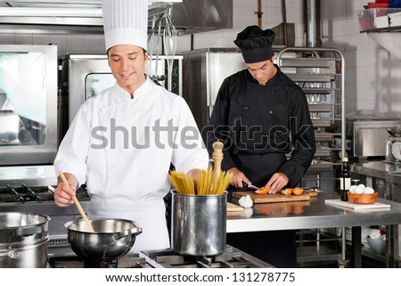 Male chef preparing food with colleague chopping carrot in industrial kitchen