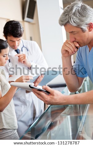 Mature male doctor reading document while colleagues standing at reception
