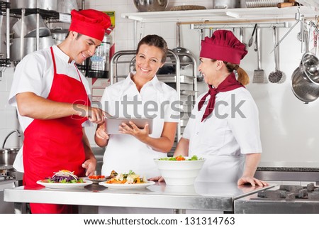 Female chef with colleagues looking for recipe on a tablet computer while cooking at kitchen
