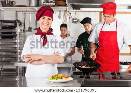 Portrait of confident female chef with colleagues cooking in industrial kitchen