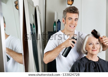 Portrait of hairdresser using hairspray to style female client\'s hair at beauty salon