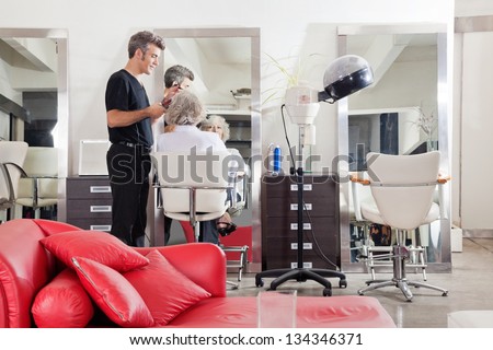Male hairstylist straightening client\'s hair at beauty salon