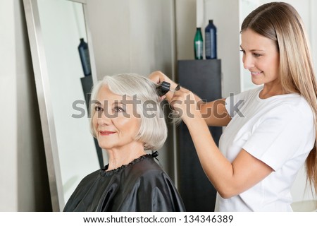 Senior woman getting her hair straightened by female hairstylist at salon