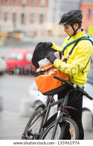 Young male cyclist in protective gear putting package in courier bag on street