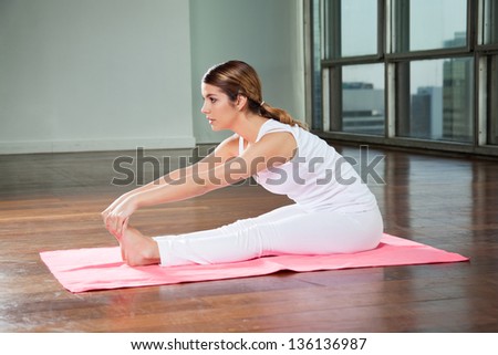 Side view of a young woman practicing yoga called Seated Forward Bend in gym