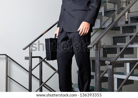 Low section of young businessman walking down the stairs at office