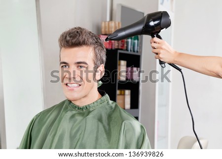 Happy male client gets his hair dried after haircut in salon