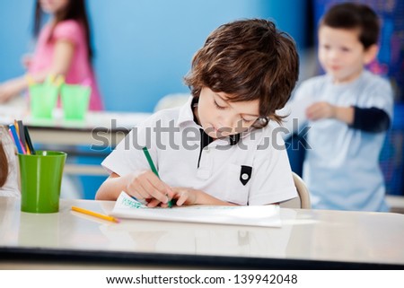 Little preschool boy drawing with sketch pen at desk in kindergarten