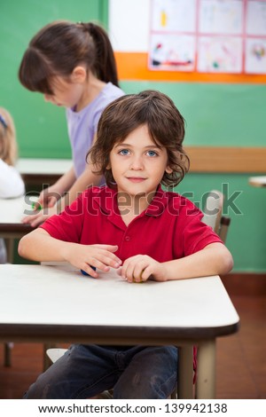 Portrait of little boy with clay while female friends playing in background at kindergarten