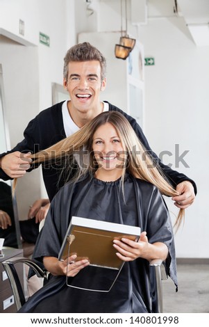Portrait of happy male hairstylist with client holding mirror at hair salon