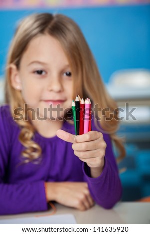 Portrait of little girl holding color pencils at desk in kindergarten
