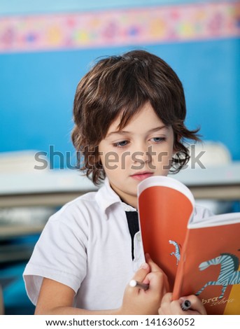 Cute little boy reading book in classroom