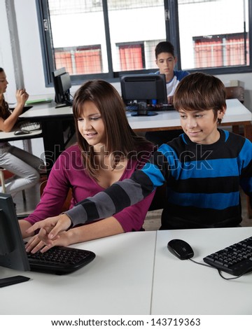 Teenage schoolboy pointing at computer monitor with classmate in lab