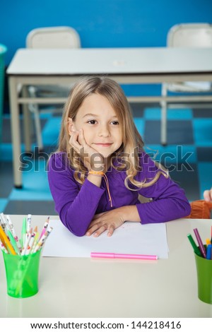 Thoughtful little girl sitting with hand on chin at desk in classroom