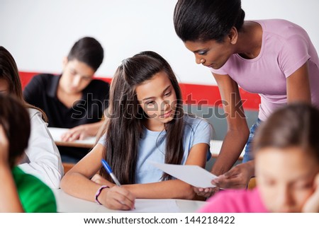 Young teacher assisting to teenage girl during examination in classroom