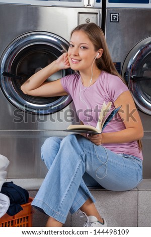 Portrait of young woman with book listening to music in laundry