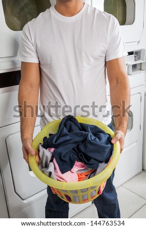 Midsection of young man with clothes basket in laundry