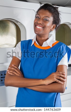 Portrait of happy young African American female helper standing with arms crossed in laundry