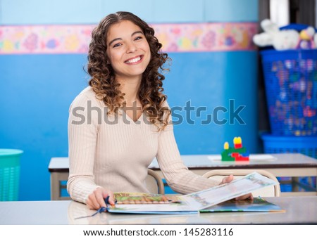Portrait of happy teacher with popup book sitting at desk in classroom