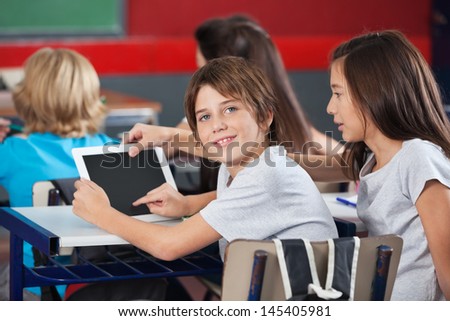 Side view portrait of little boy with girl using digital tablet at desk in classroom