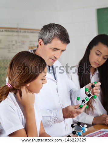 Mature male teacher explaining molecular structure to female students at desk in lab