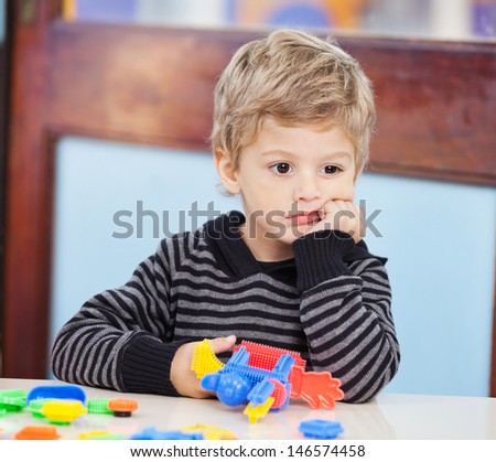 Thoughtful little boy with blocks looking away in preschool