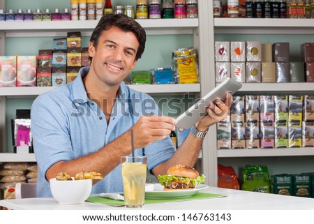 Portrait of male customer with digital tablet and snacks at table in grocery store