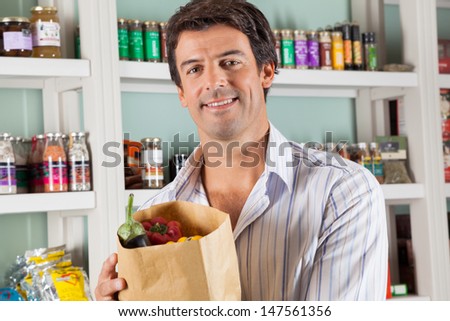 Portrait of handsome male customer with vegetable bag standing against shelves in supermarket